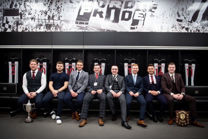 Colour photo of 8 smartly dressed young men, two of them with trophies