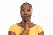Professional headshot of Ngunan Adamu wearing a yellow top. Ngunan is looking upwards and has he hand to her chin posing as if she is thinking. Ngunan also wears large hooped earrings and red lipstick.