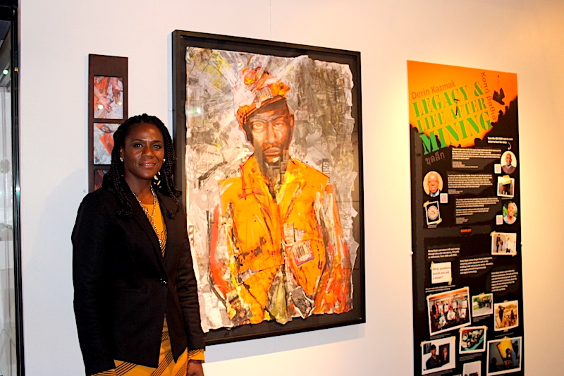 Image of Norma Gregory standing next to artwork that features in the exhibition. Next to the artwork is a information panel which has both text and small images on.