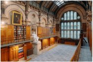 A photo of The Common Room's Wood Hall. Wide lens shot from the balcony. A large stained glass window is in the background, and wooden bookcases and panels, plus long golden balconies, line the room down towards the window. In the centre of the shot, half way down the room, is a large statue of Nicholas Wood on a plinth - the Hall's namesake.