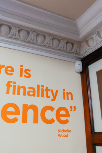 A photograph taken in The Common Room' Lecture Theatre. To the right of the photo, orange text on a wall reads '