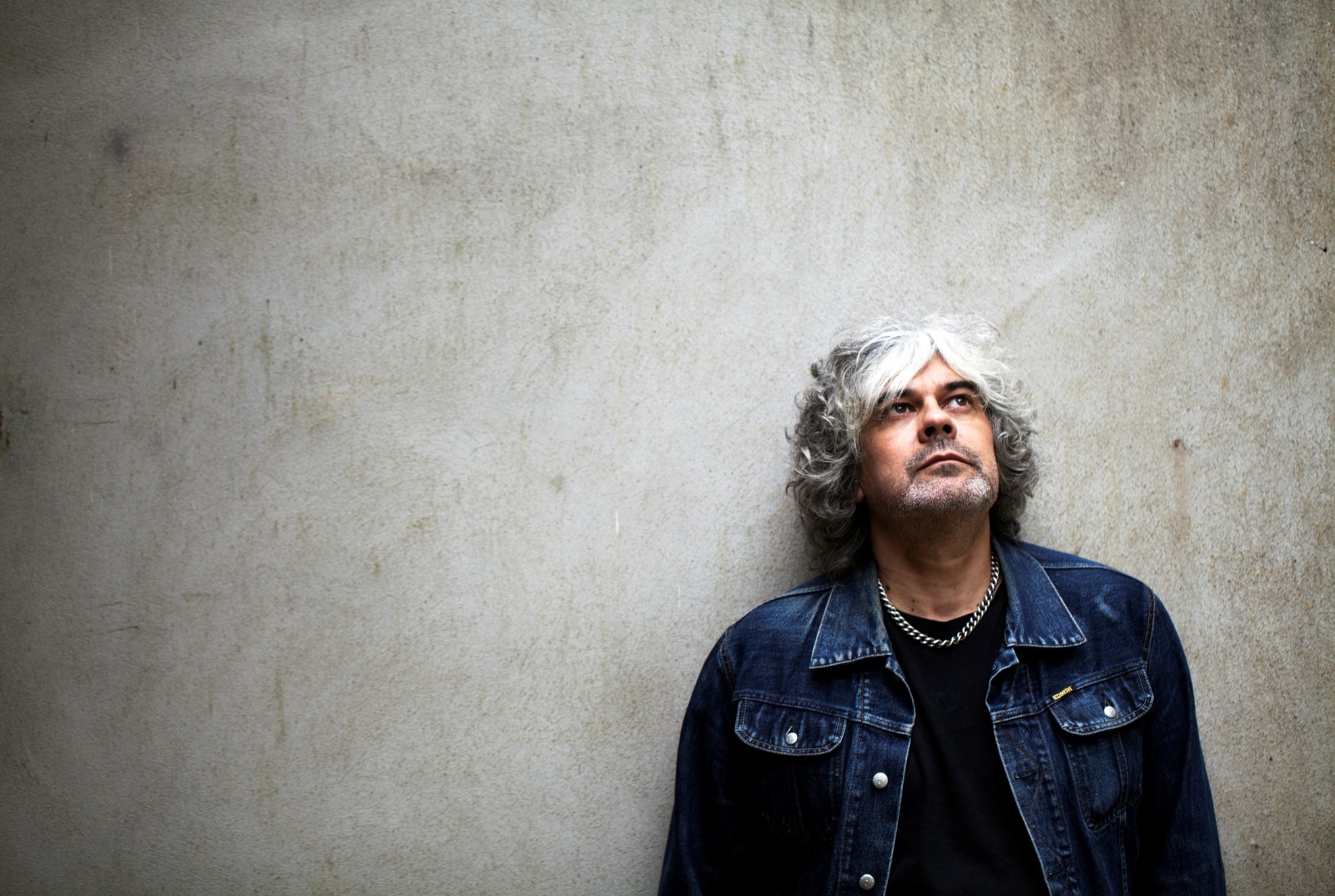 A photgraph of Matt Deighton wearing a blue denim jacket, leaning against a grey wall